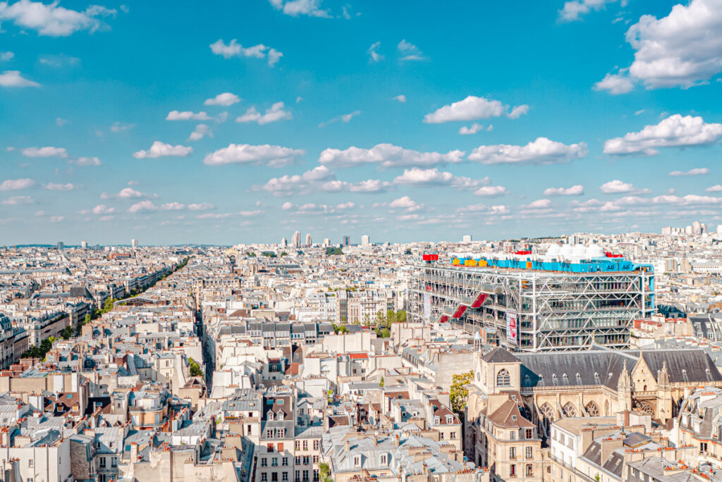 Une vue du Centre Pompidou depuis la Tour Saint-Jacques à Paris, qui domine le paysage urbain de la ville. Le Centre Pompidou se distingue par ses structures métalliques et colorées, qui contrastent avec les immeubles haussmanniens et les églises. Un symbole de l’art moderne au milieu du patrimoine historique.